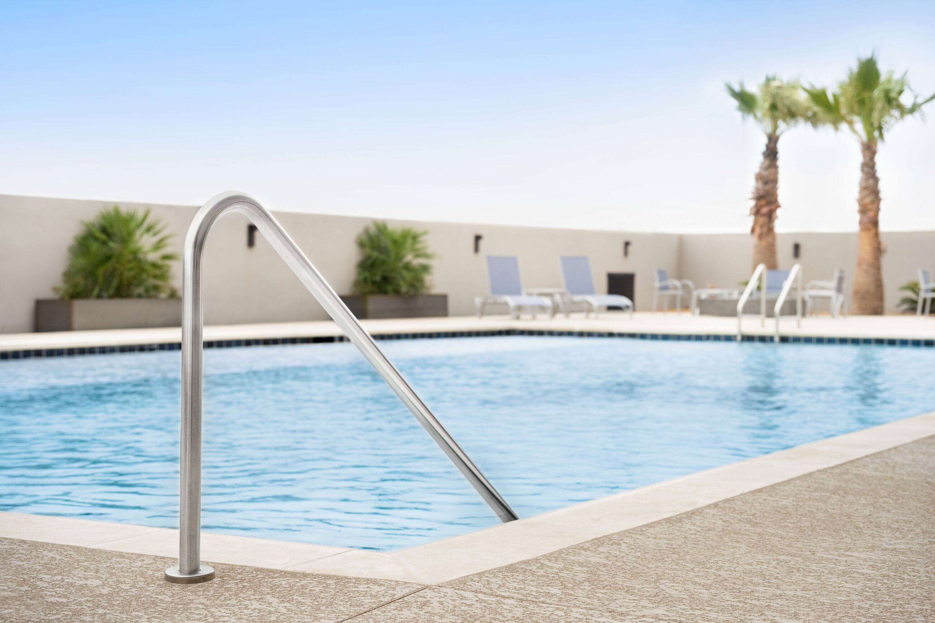 A swimming pool with a metal ladder, lounge chairs, and palm trees.