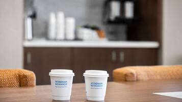 Deux tasses à café portant le logo « Wyndham Rewards » sont posées sur une table en bois dans une pièce où l’on aperçoit une cuisine en arrière-plan.