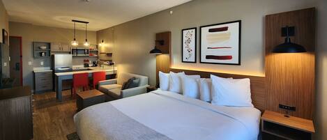 A hotel room with a large bed, a desk, a chair, and a kitchenette.