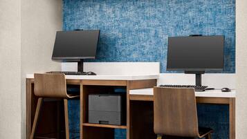 A modern office space with two desks, each with a computer monitor, keyboard, and mouse. There are two chairs, and a printer is visible on the left desk.
