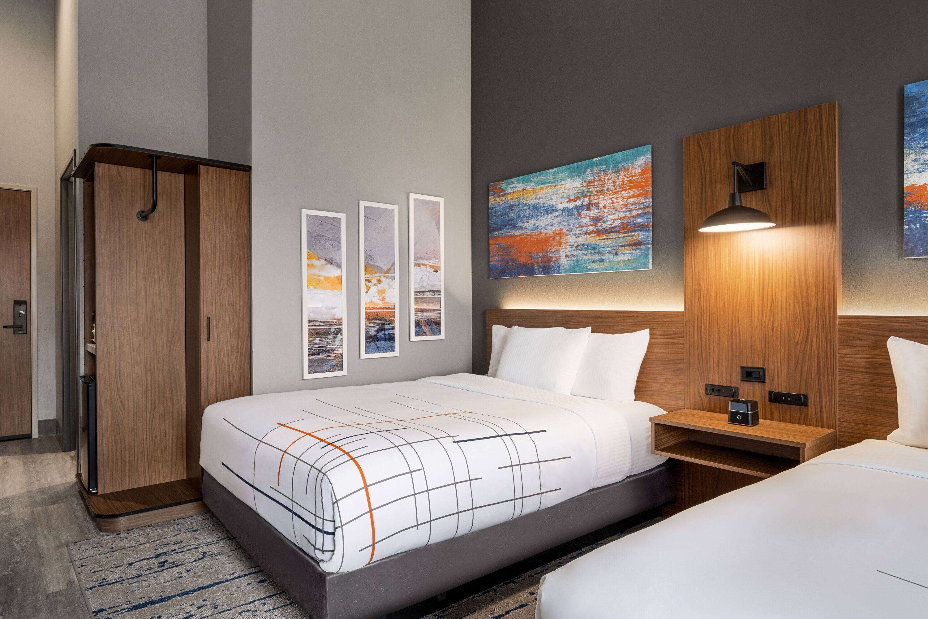 Una habitación de hotel moderna con una cama grande, un armario y una mesita de noche con lámpara.
