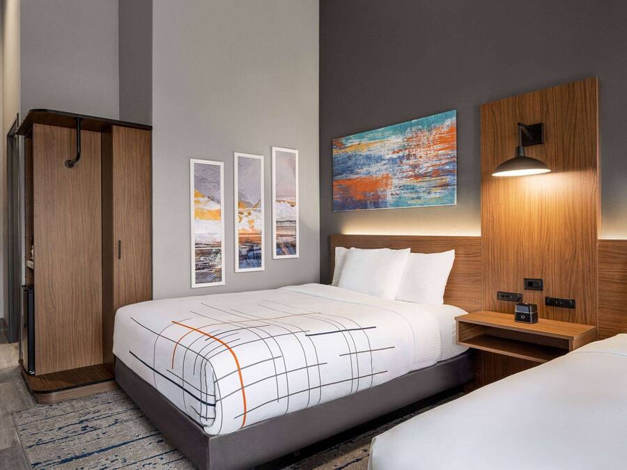 Una habitación de hotel moderna con una cama grande, un armario y una mesita de noche con lámpara.