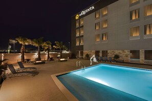 A hotel with a swimming pool, lounge chairs, and palm trees.
