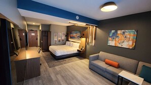 A modern hotel room with a bed, a sofa, a desk, and artwork on the walls. - La Quinta Inn & Suites by Wyndham Del Rio (Del Rio)