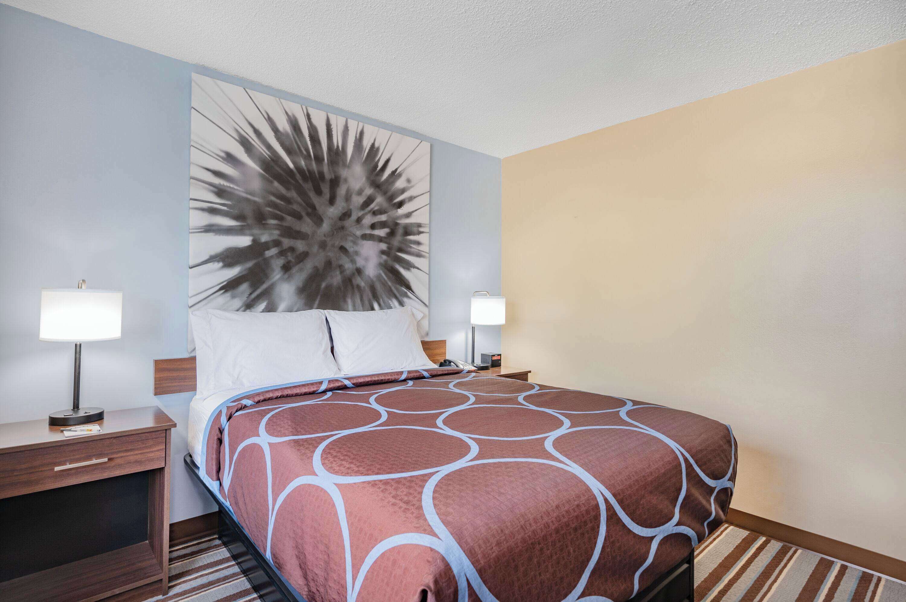 Una habitación de hotel con una cama grande, dos mesitas de noche con lámparas, un cabecero con un panel decorativo y una alfombra a rayas.