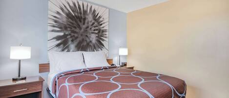 Una habitación de hotel con una cama grande, dos mesitas de noche con lámparas, un cabecero con un panel decorativo y una alfombra a rayas.