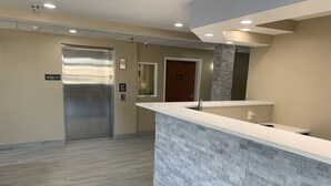A reception area with a modern design, including a reception desk, a glass elevator, and a door marked "106-117". - Super 8 by Wyndham Joliet (Joliet)