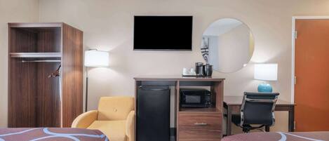 Quarto de hotel com duas camas, uma mesa com computador, micro-ondas, frigorífico, uma cadeira, guarda-roupa, televisão e espelho.