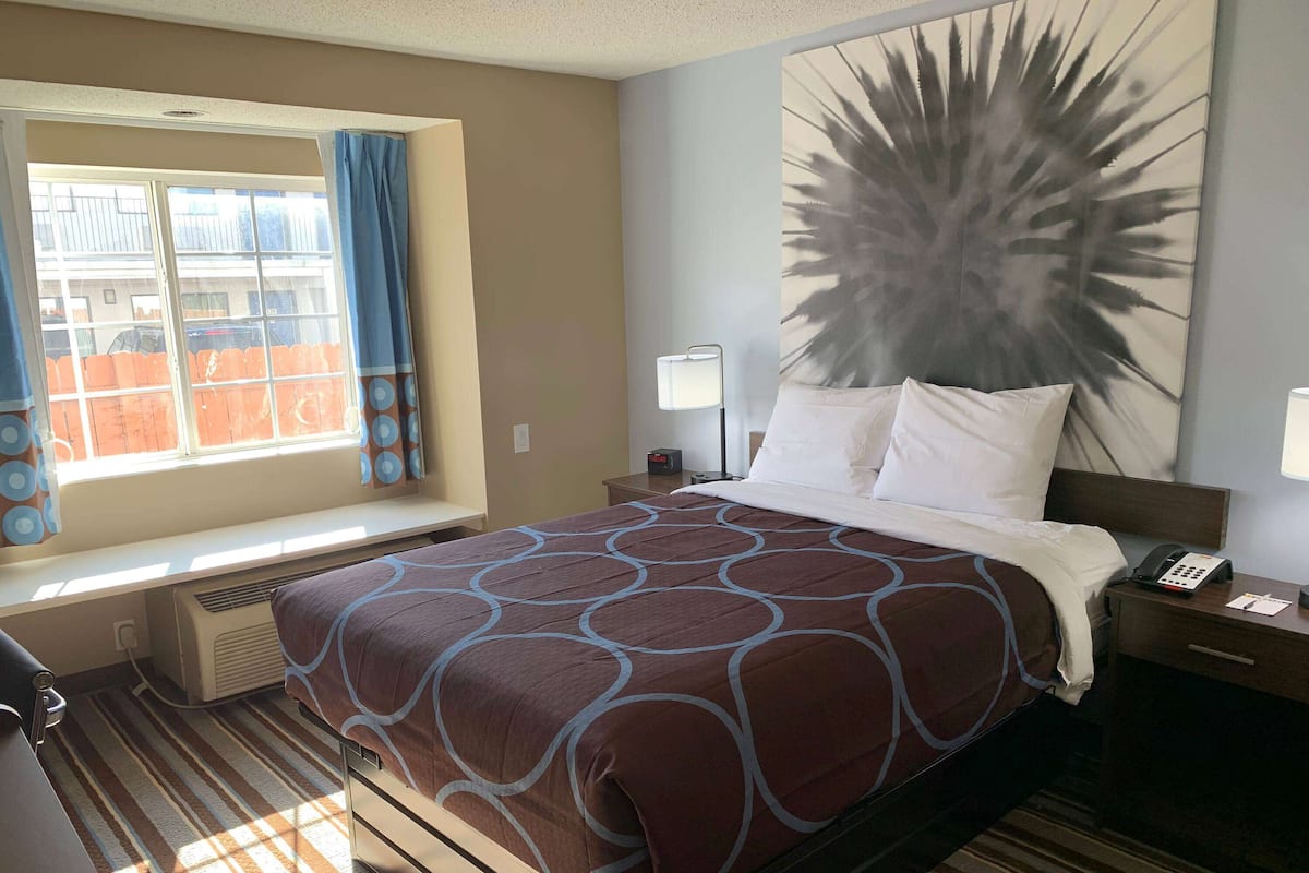 Hotelkamer met een groot bed, een raam met gordijnen, een wanddecoratie, een nachtkastje met een lamp en een telefoon.