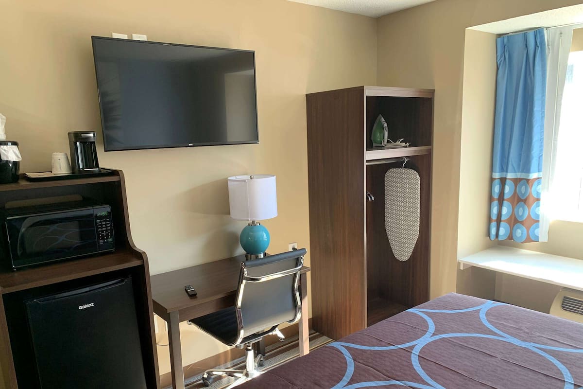 Hotelkamer met een bed, een bureau met stoel, een televisie, een magnetron, een koelkast, een koffiezetapparaat en een raam met gordijnen.
