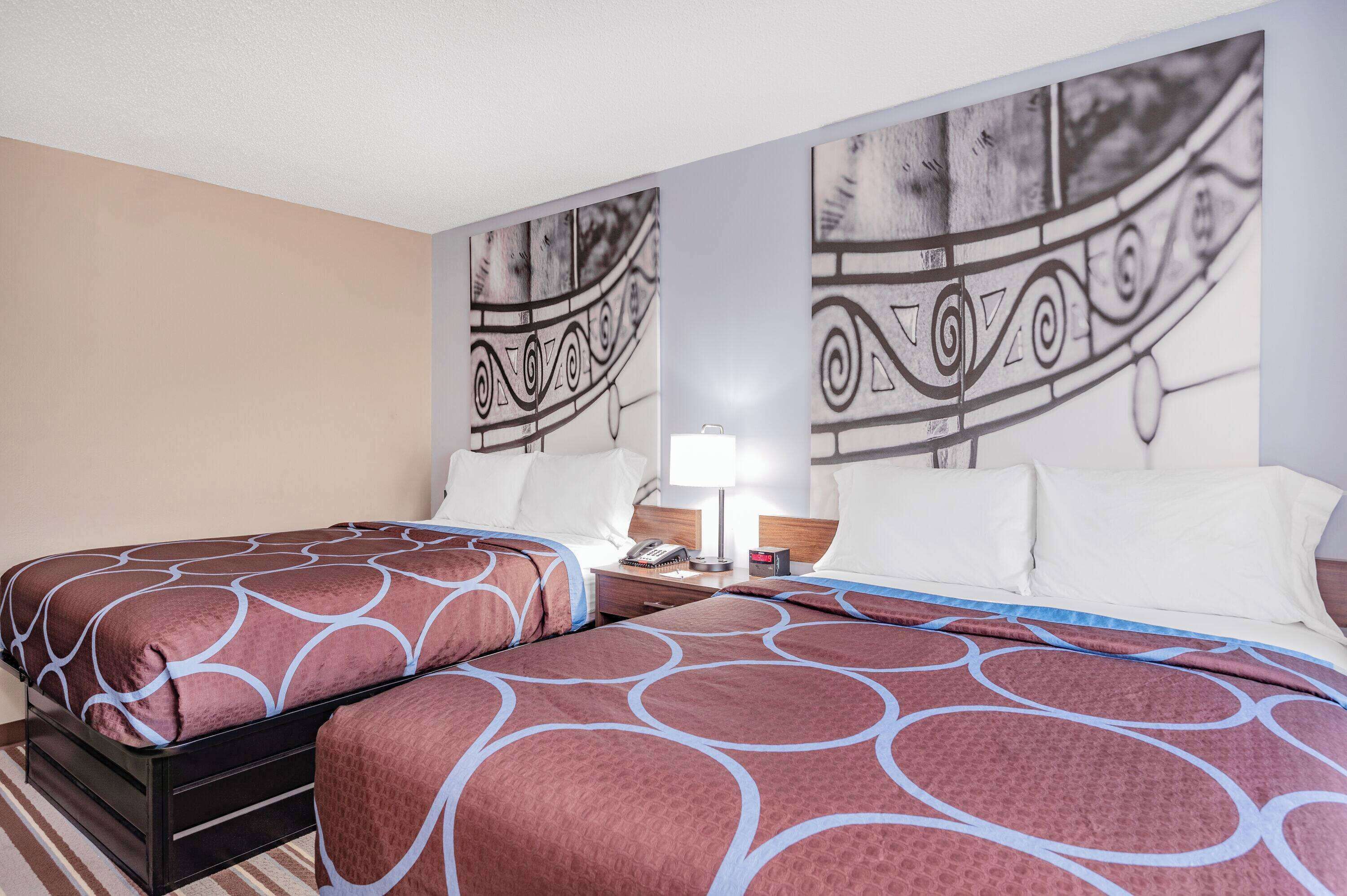 Une chambre d’hôtel avec deux lits, une table de chevet, une lampe et un mur orné d’un motif décoratif.
