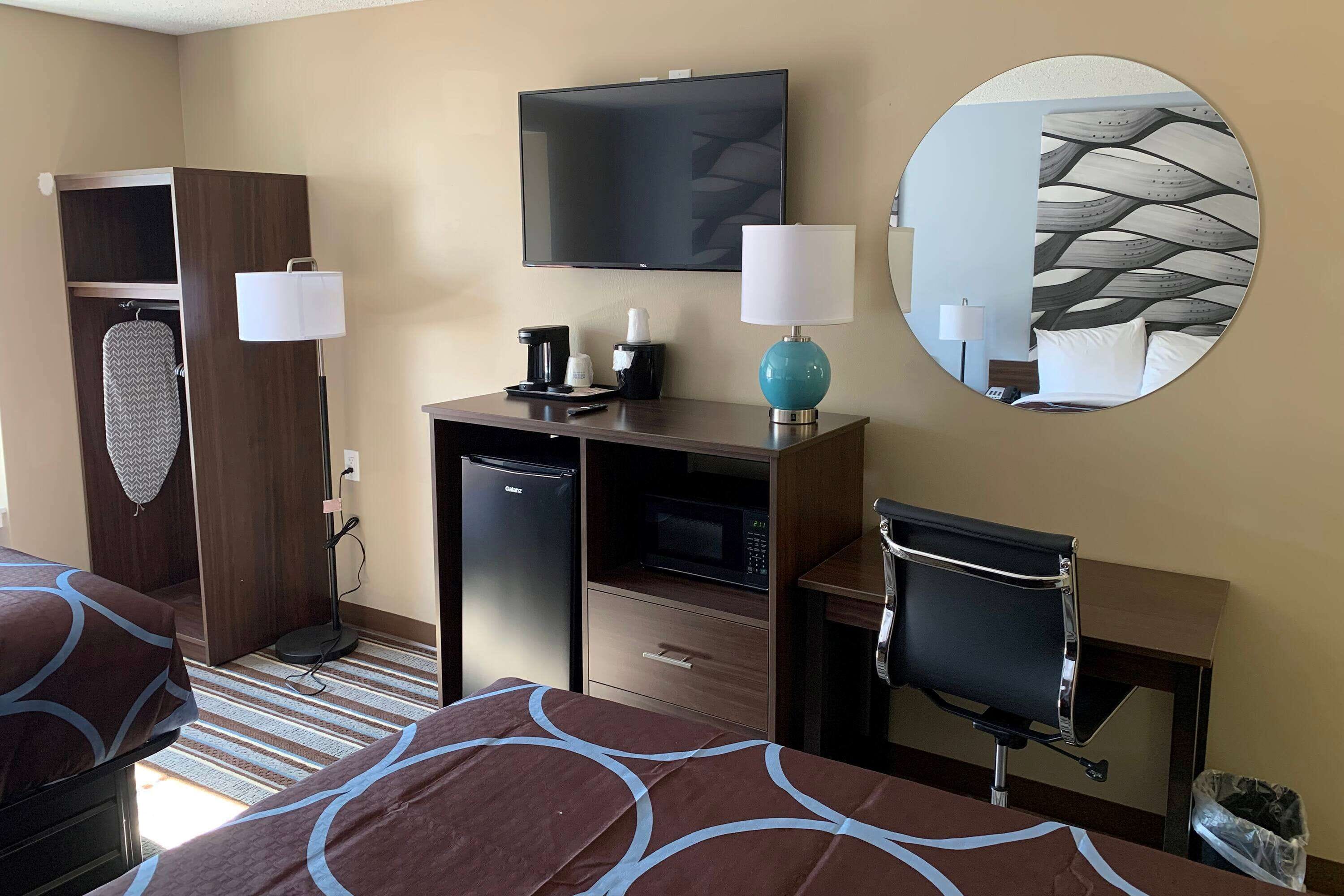 A hotel room with a bed, desk, chair, television, and a mirror.