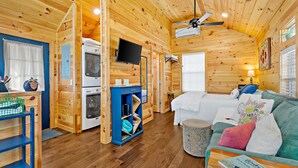 Interior acogedor de una cabaña con detalles de madera, un sofá, un televisor y una kitchenette.