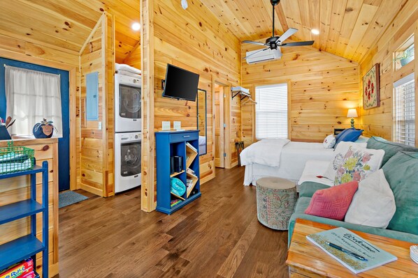 Un intérieur de chalet chaleureux, avec un revêtement en bois, un canapé, un téléviseur et un coin cuisine.