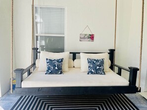 A bed with a swing seat, a window with blinds, and a welcome sign.