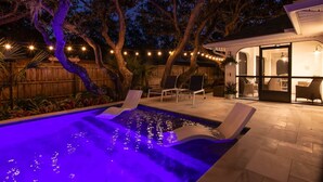Una piscina con fuente, rodeada de sillas de descanso e iluminación con luces colgantes.