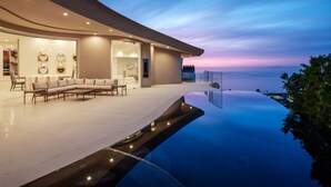 A modern house with a curved roof, a large living area with a sofa and chairs, and a pool overlooking the ocean. - La Jolla villa with 5 bedrooms, private pool, hot tub, and ocean views. (La Jolla)