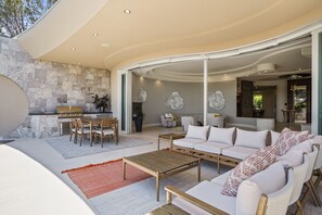 A modern living room with a stone wall, a dining area, and a kitchen with a grill. - La Jolla villa with 5 bedrooms, private pool, hot tub, and ocean views. (La Jolla)