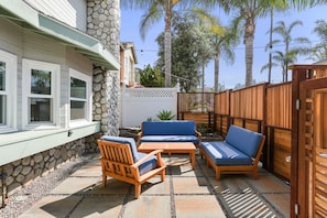 A patio with wooden furniture, a stone wall, and a wooden fence. - Single Family | Walk to Beach + Dining | Roof Deck (La Jolla)