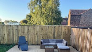 A backyard with a wooden fence, a blue chair, a gray sectional sofa, and a small table. - 3 bedroom accommodation in Fraisthorpe, near Bridlington (Fraisthorpe, near Bridlington)