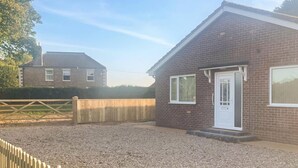 A brick house with a white door and windows, a gravel driveway, and a wooden fence. - 3 bedroom accommodation in Fraisthorpe, near Bridlington (Fraisthorpe, near Bridlington)