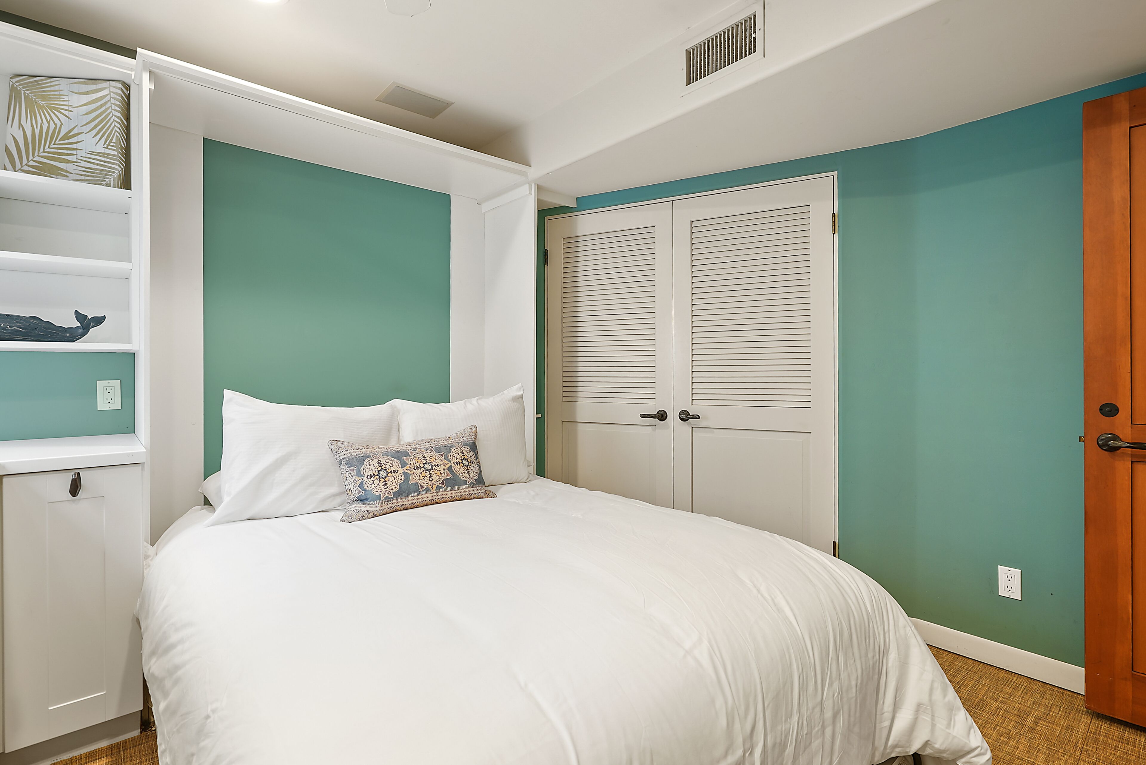 Une chambre à coucher avec un lit, une armoire blanche et une étagère ornée d’objets décoratifs.