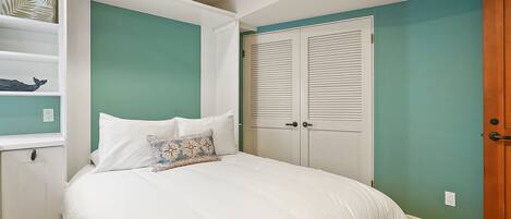 A bedroom with a bed, white wardrobe, and a shelf with decorative items.