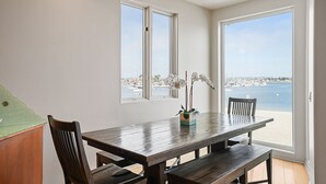 Ein Essbereich mit Holztisch und Stühlen, großen Fenstern mit Meer- und Stadtblick sowie einer Topfpflanze auf dem Tisch.