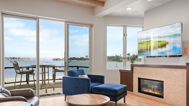 Ein modernes Wohnzimmer mit Kamin, großem Fernseher und Blick auf das Wasser.