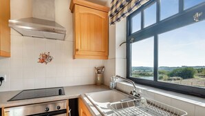 Eine Küche mit Herd, Backofen und Spüle, Holdschränken und einem Fenster mit Blick.