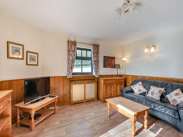 A cozy living room with a wooden TV stand, a leather sofa, and a wooden coffee table. - Viking Cottage - UK36662 (Belchford)