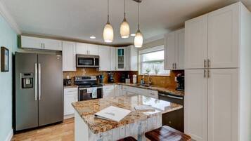 A modern kitchen with white cabinets, a granite countertop, a built-in oven, a microwave, and pendant lighting.