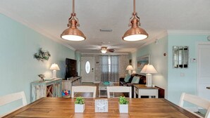 Een eetgedeelte met een houten tafel en stoelen, twee hanglampen, en uitzicht op de woonkamer.