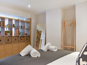 Une chambre bien rangée, avec un lit, une armoire en bois, un miroir et un étendoir en bois.