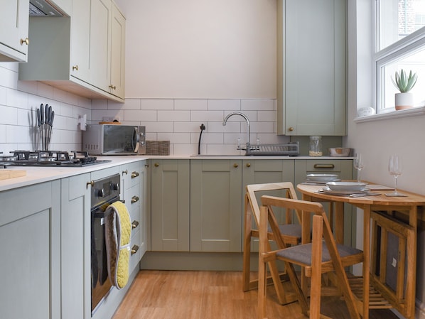 Une cuisine compacte équipée d’un four à micro-ondes, d’une cuisinière, d’un évier et de chaises en bois disposées autour d’une petite table.