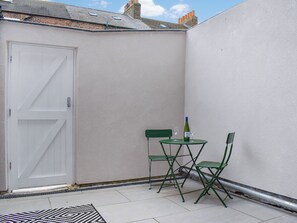 Une petite terrasse extérieure avec une porte blanche, une table pliante verte, deux chaises et une bouteille de vin.