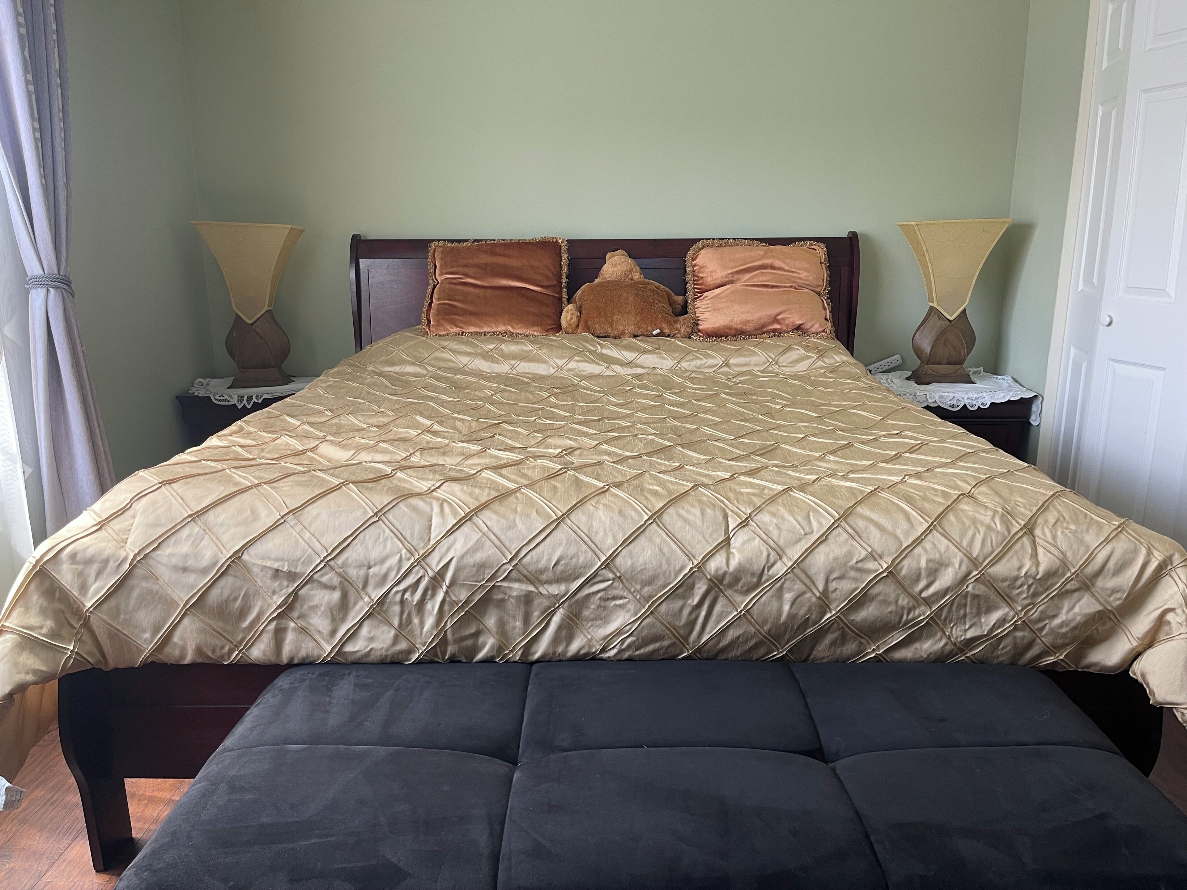 A bed with a quilted gold cover, two bedside lamps, and a dark bench at the foot of the bed.
