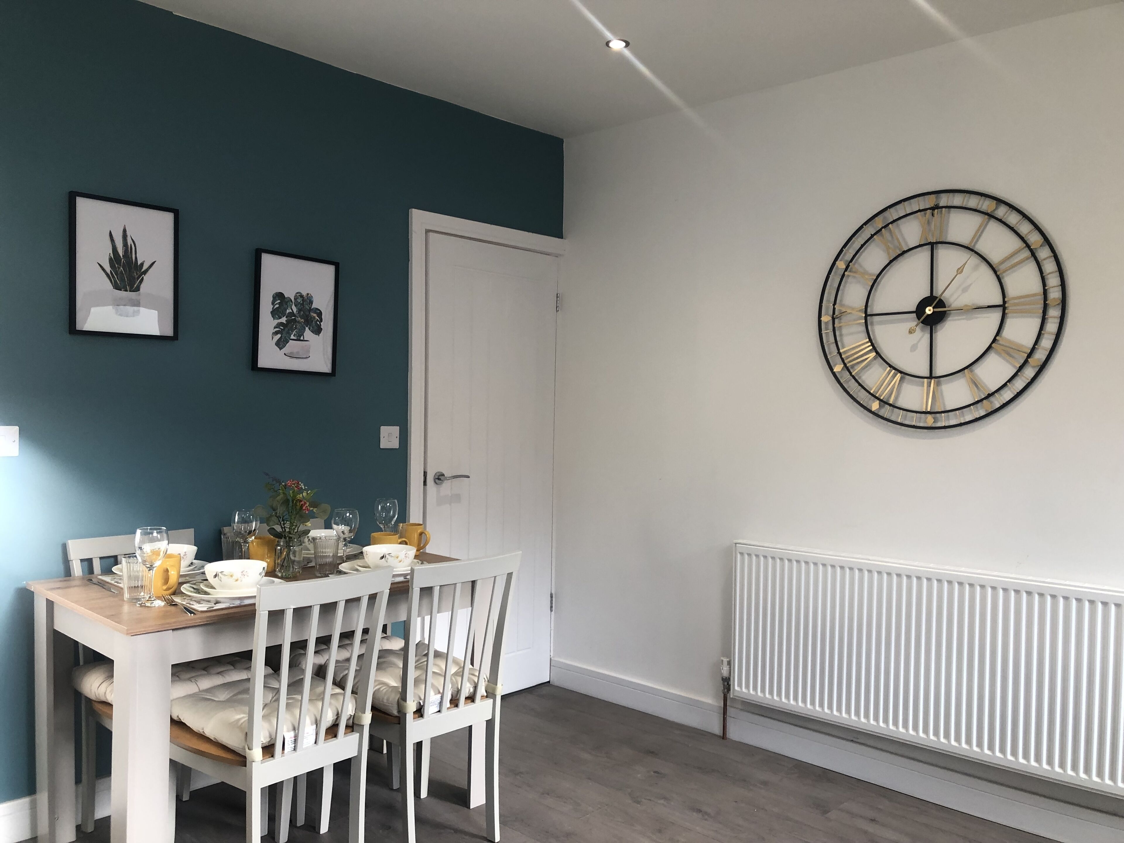 A dining area with a white table and chairs, a white radiator, and a wall clock.