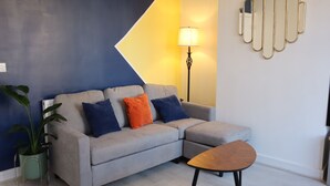 Un salon moderne avec un canapé d’angle gris, une petite table basse en bois, un lampadaire et un miroir décoratif accroché au mur.
