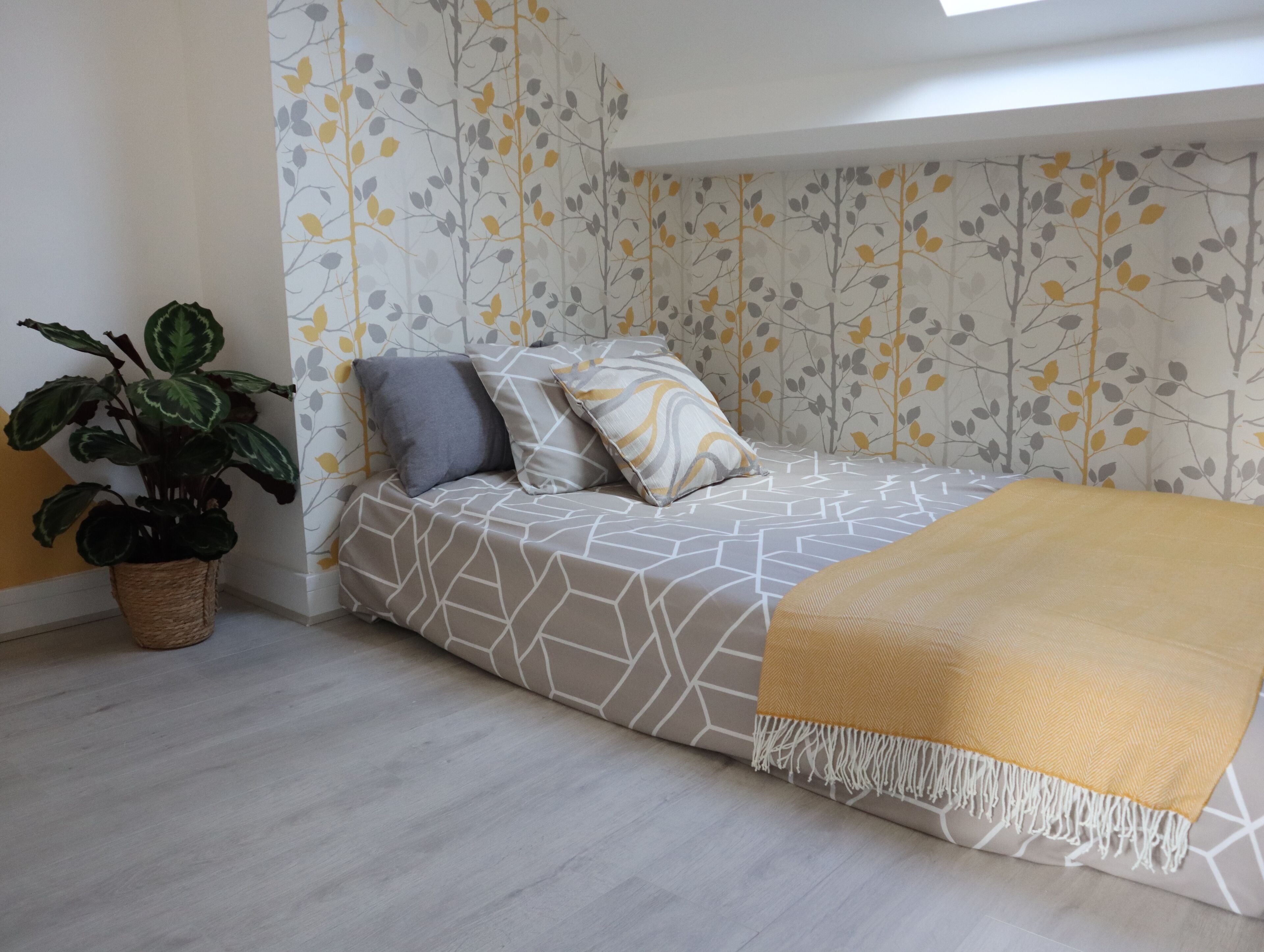 A bedroom with a bed, a potted plant, and a patterned wallpaper.