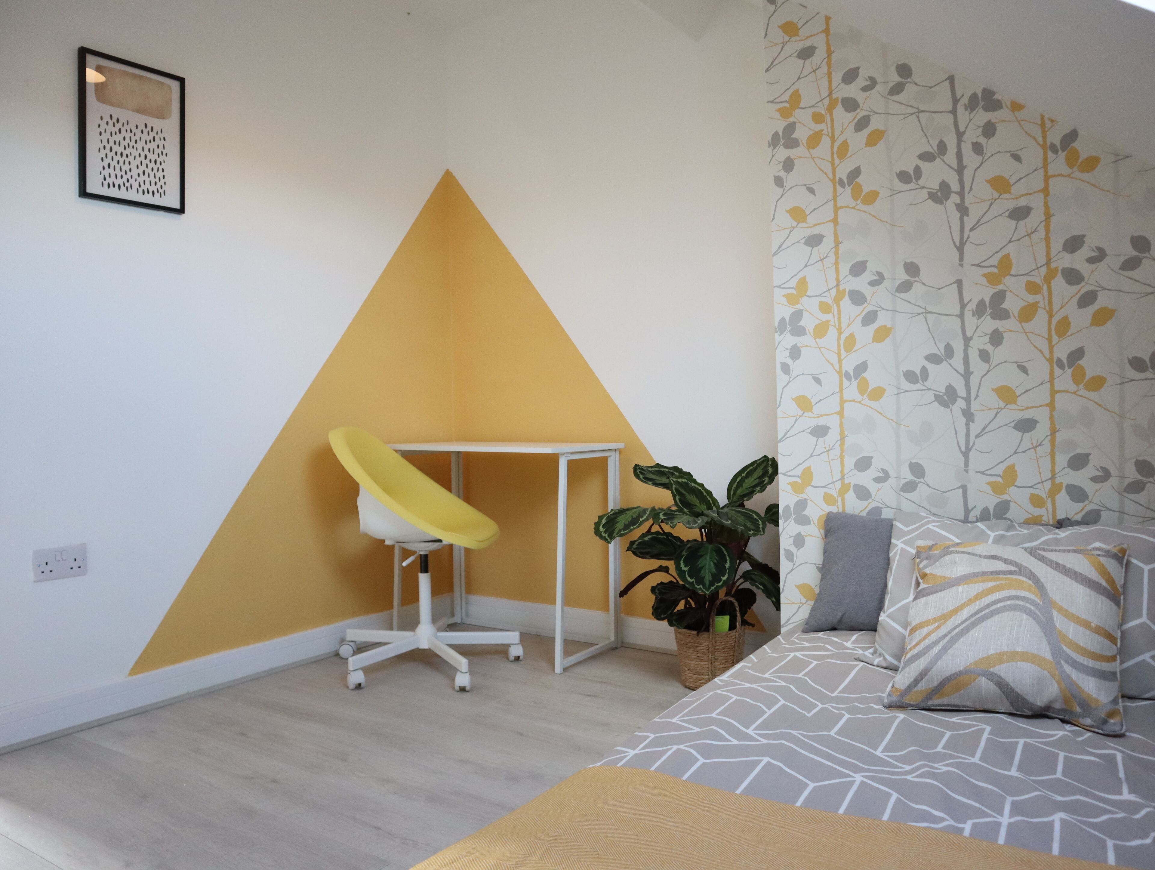 A room with a bed, a desk, and a potted plant.