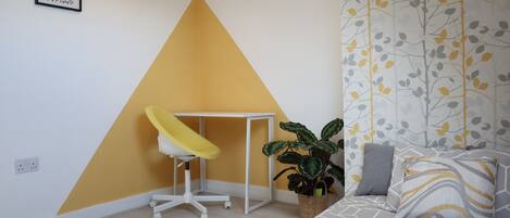 A room with a bed, a desk, and a potted plant.