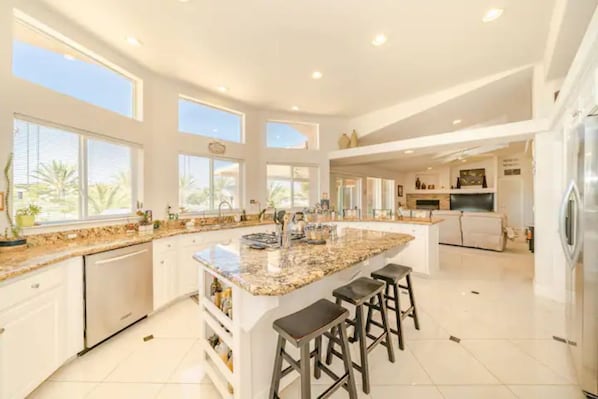 A spacious kitchen with a large island, white cabinetry, and ample natural light from large windows.