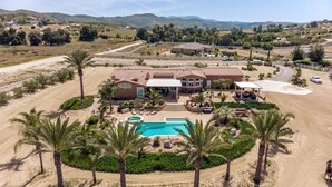 A large house with a swimming pool, surrounded by palm trees and a dirt road. - Beautiful Villa located in Temecula Wine Country (Temecula)