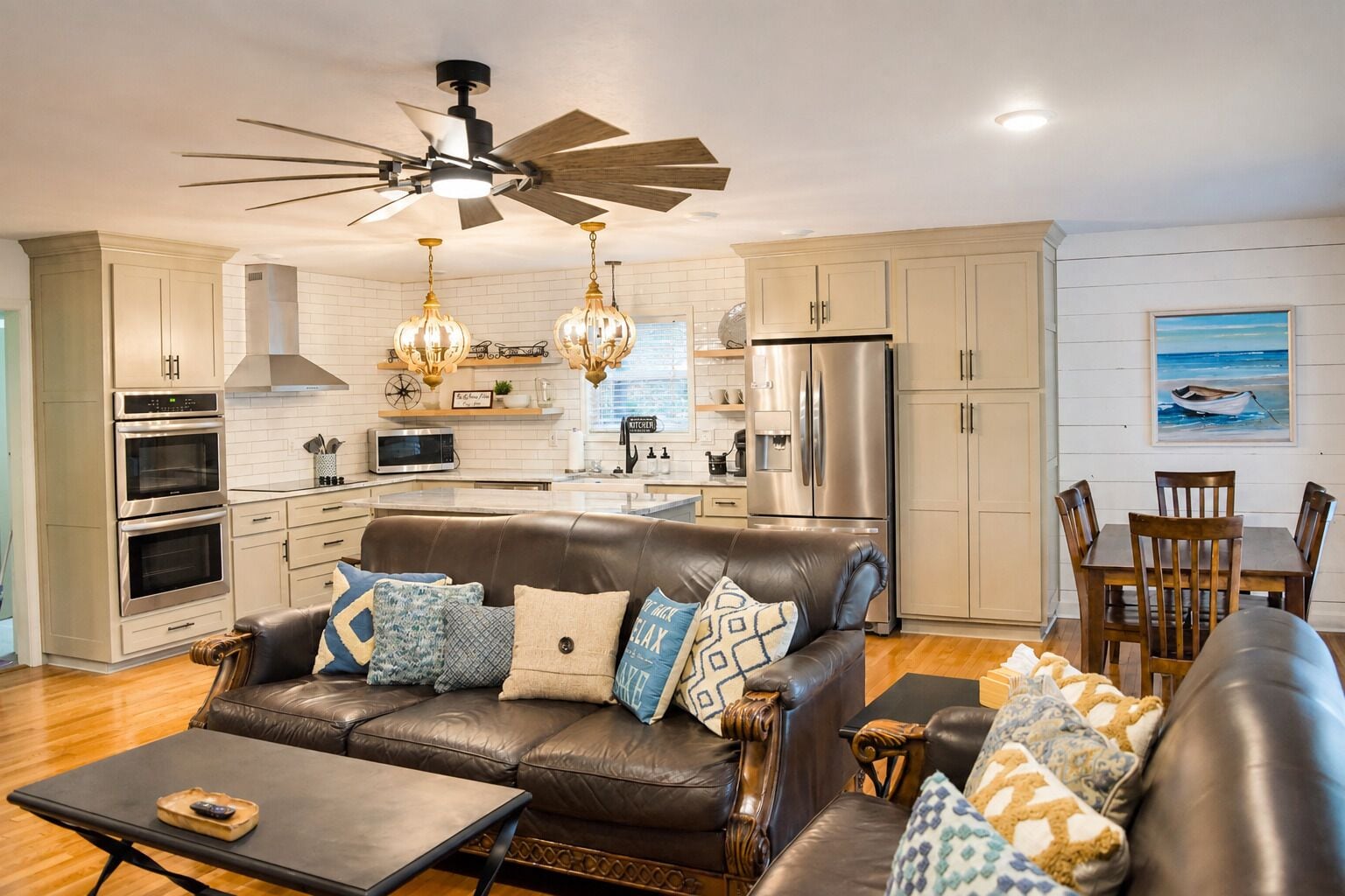 A modern kitchen with stainless steel appliances, a dining area with wooden furniture, and a living room with a leather sofa.
