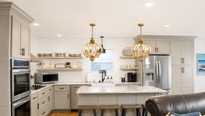 Cocina moderna con armarios blancos, electrodomésticos de acero inoxidable, una isla de mármol y dos taburetes de bar.