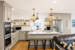 Cocina moderna con armarios blancos, electrodomésticos de acero inoxidable, una isla de mármol y dos taburetes de bar.