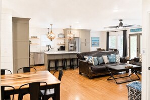 Une cuisine moderne dotée d’un îlot central, de tabourets de bar, d’une table à manger avec des chaises, d’un canapé en cuir agrémenté de coussins décoratifs et d’un ventilateur de plafond.