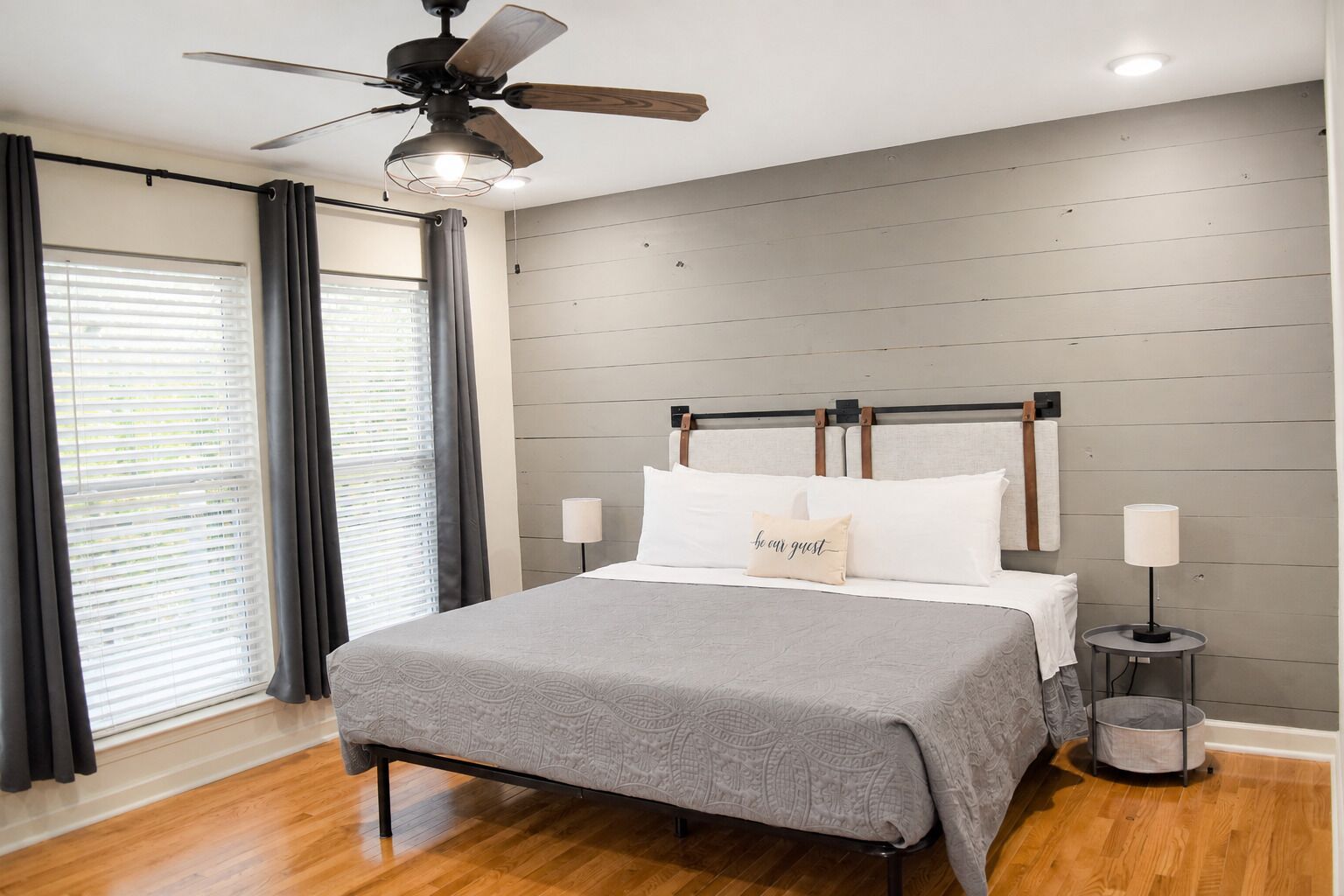 Une chambre à coucher avec un lit, un ventilateur de plafond, une table de chevet avec une lampe et une fenêtre avec des rideaux.