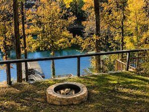 Un espacio al aire libre frente al lago, con un brasero de piedra y barandilla de metal con vista al agua.